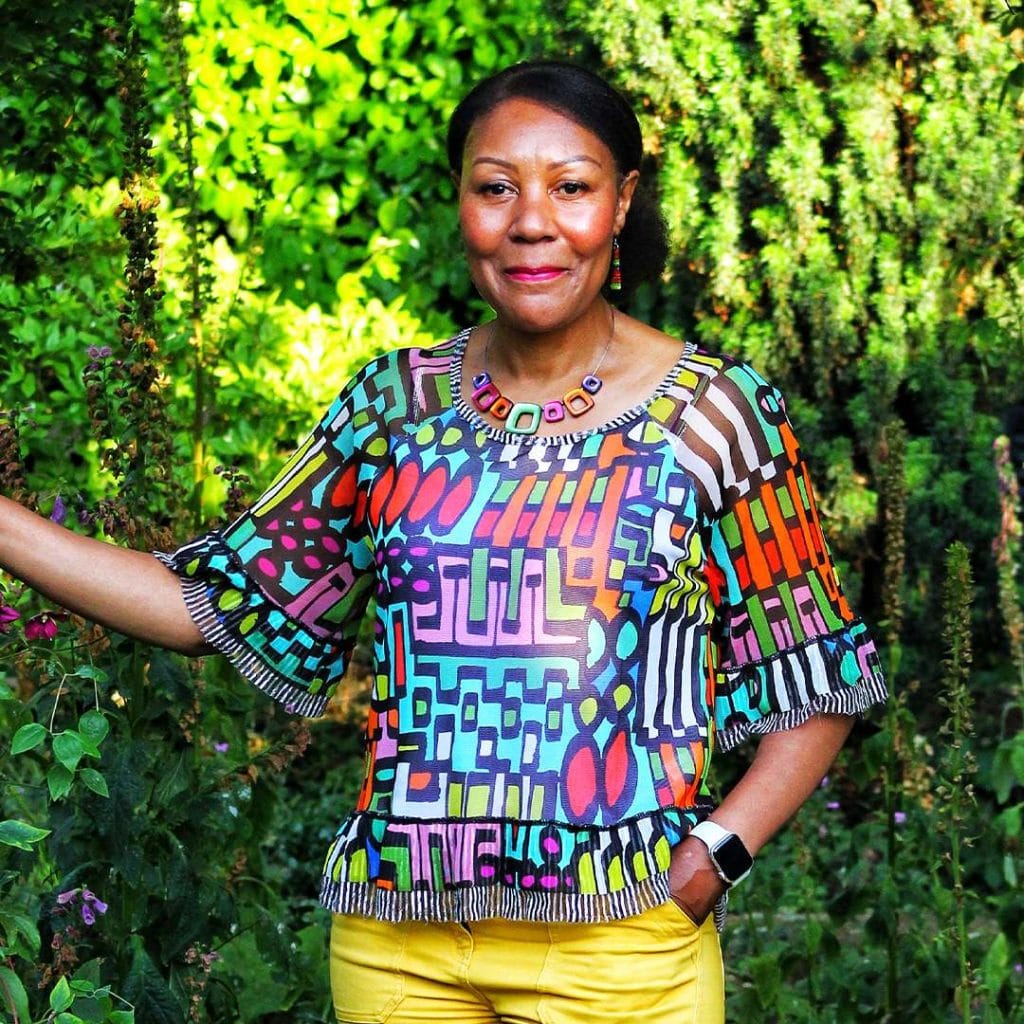 A portrait photo of Andrea in a garden, wearing iconic colours, smiling at the camera.