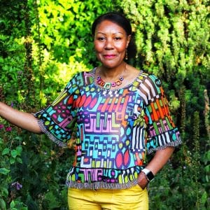 A portrait photo of Andrea in a garden, wearing iconic colours, smiling at the camera.
