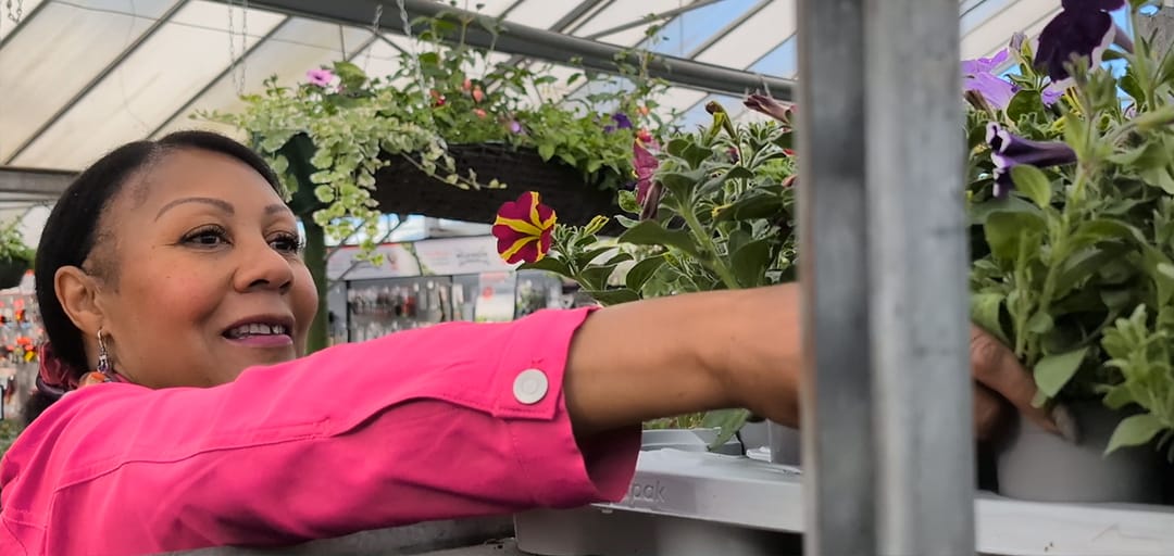 Andrea in her local garden centre, reaching for some plants in a pot.