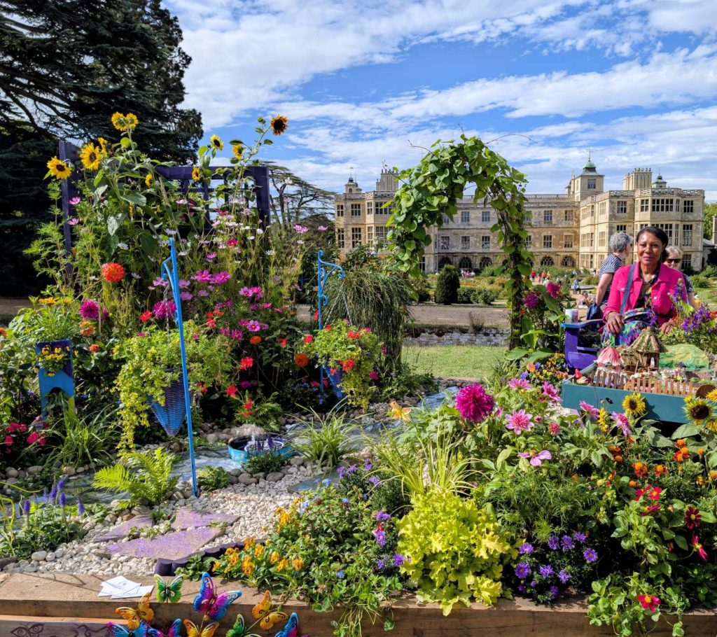 A photo featuring Andrea sitting in her Wonderland Garden design in front of Audley End House at BBC Gardener's World Autumn Fair 2026.